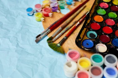 Renkli resimlerin düz yatışı, mavi arkaplanda palet ve fırçalar, sanat, resim ve hobi konsepti, üst görünüm, kopyalama alanı.