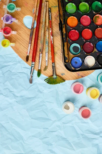 Flat lay of colorful paints, painting palette and brushes on blue background, art, painting and hobby concept, top view, copy space