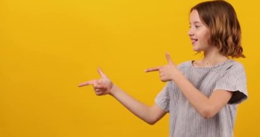 Neşeli, pozitif on yıllık genç kız sarı arka plandaki stüdyoda izole edilmiş çalışma alanını işaret ediyor, mesaj üstüne mesaj yazıyor, taklit ediyor.