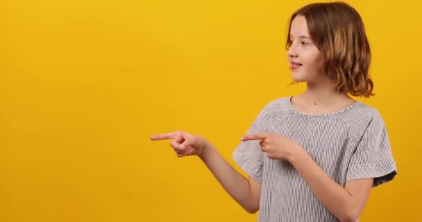 快乐的 积极的10岁少女把手指指向被黄色背景工作室隔离的工作区 复制文本空间 — 图库视频影像