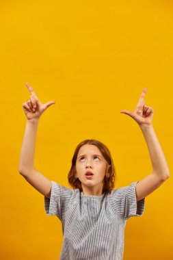 Neşeli, pozitif on yıllık genç kız sarı arka plan stüdyosunda izole edilmiş çalışma alanını işaret ediyor, mesaj üstüne mesaj yazıyor, taklit ediyor.