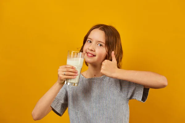 stock image Pretty teen girl, child with a fresh glass of milk isolated on studio yellow background, strong bones, milk for growth, healthy lifestyle concept, copy space