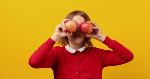 黄色のスタジオの背景に彼女の目の前でリンゴを保持スタイリッシュな笑顔の学校の十代の女の子 学校のコンセプトに戻る 目の健康 — ストック動画