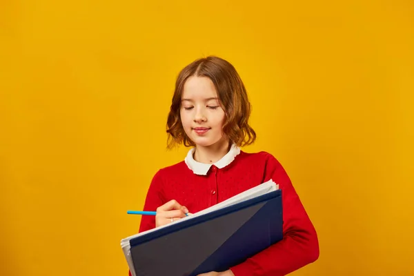 沉思学校的少女拿着笔 在笔记本上写着黄色的工作室背景 回到学校的概念 — 图库照片