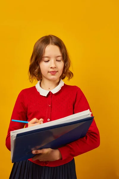 沉思学校的少女拿着笔 在笔记本上写着黄色的工作室背景 回到学校的概念 — 图库照片