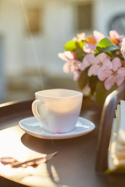 Bir fincan kahve çiçeği ve defter, terasta küçük siyah masanın üzerinde güneşli bir günde, açık havada çalışma alanı, yaz tatili, kahve molası..