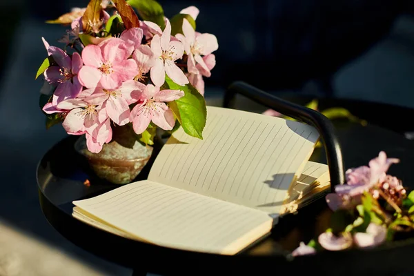 Open notebook and flowers and on the small black table on terrace at home in a sunny day, hardlight, outdoor workspace, summer relaxation, notes, ideas, plannin