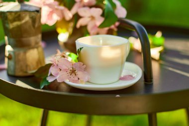 Bir fincan kahve çiçeği ve defter, terasta küçük siyah masanın üzerinde güneşli bir günde, açık havada çalışma alanı, yaz tatili, kahve molası..