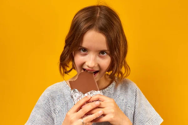 Красивая Девушка Подросток Ест Кусает Шоколадку Изолированы Студийном Желтом Фоне — стоковое фото