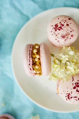 Mavi arka planda çeşitli tatlı Fransız pembe badem kurabiyeleri. Taze çiçekler, hamur işleri, tatlı hoşgörü..