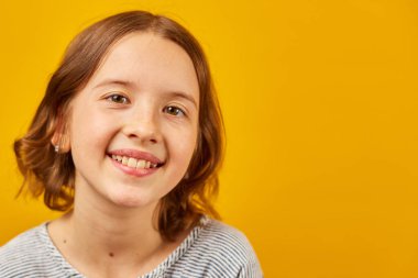 Stüdyonun sarı arka planında mutlu bir genç kız portresi, pozitif duygu yaşam tarzı