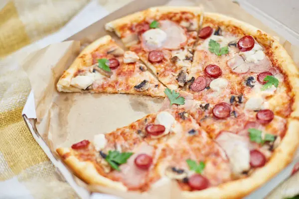 A freshly baked pizza with sliced tomatoes, cheese, mushrooms, and herbs is missing two slices, suggesting a shared meal at an outdoor picnic.