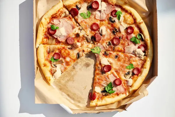 A freshly baked pizza with sliced tomatoes, cheese, mushrooms, and herbs is missing two slices, suggesting a shared meal at an outdoor picnic.