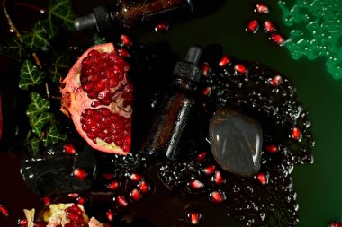 Canlı nar tohumları ve dilimlerinin arasına yerleştirilmiş koyu cam damlatan yağ şişesinin yakın plan görüntüsü, doğal ve bütünsel bir sağlık temasını vurguluyor..