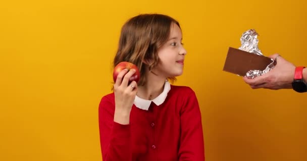 Young Girl School Uniform Opts Apple Declining Chocolate Bar Promoting — Stock Video
