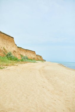 Kumlu sakin sahil şeridi, aşınan uçurumlar ve mavi gökyüzünün altında sakin deniz..