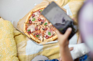 Genç bir kız, tek kolunda alçı varken telefonla lezzetli bir pizzanın fotoğrafını çeker..