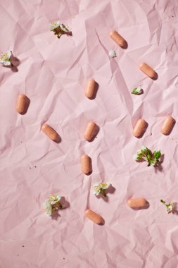 Blister packs with capsules scattered on a textured pink background, alongside small white flowers. clipart