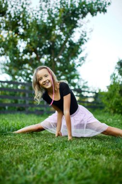 Akşamın erken saatlerinde çimenli bir bahçede jimnastik yapan gülümseyen kız..
