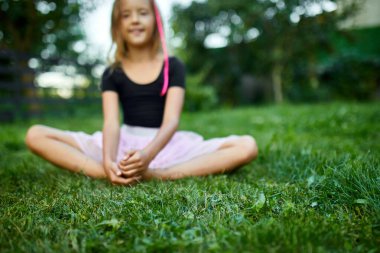 Gülümseyen bir kız yaz boyunca neşeli bir ifadeyle çimenlerde oturur..