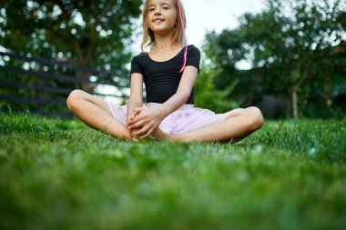 Gülümseyen bir kız yaz boyunca neşeli bir ifadeyle çimenlerde oturur..