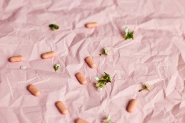 Blister packs with capsules scattered on a textured pink background, alongside small white flowers. clipart