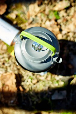 Çaydanlığı olan taşınabilir bir soba ormanda yerde oturur, güneş ışığı ağaçların arasından süzülür. Çaydanlık ısıtma suyudur, açık hava yemekleri veya çay için idealdir..