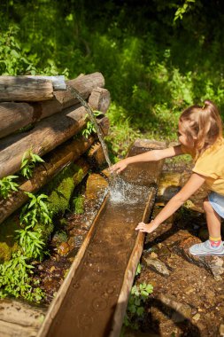 Genç bir kız, güneşli bir günde serinlemek için yüzüne su sıçratan doğal bir pınarın yanında durur. Yeşilliklerle çevrili, doğada keyifli bir anın tadını çıkarıyor..