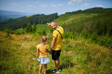 Bir baba ve kızı dağlarda bir anı paylaşıyor, manzaraya bakıyor. Doğada birlikte vakit geçirmekten, anılar inşa etmekten ve patikaları keşfetmekten hoşlanırlar..