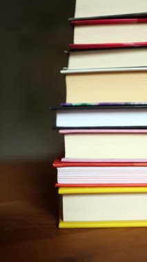 Ahşap bir masanın üzerine düzgünce istiflenmiş renkli kitaplardan oluşan bir derleme. İçlerindeki hikayeleri araştırmaları için bir sıcaklık hissi uyandırıyor ve okuyucuları davet ediyor..