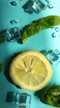 Limon dilimleri, taze fesleğen yaprakları ve buz küpleri parlak mavi bir yüzeye serin ve ferahlatıcı bir yaz atmosferini çağrıştıran içecekler için mükemmel bir şekilde düzenlenmiştir..
