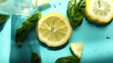 Limon dilimleri, taze fesleğen yaprakları ve buz küpleri parlak mavi bir yüzeye serin ve ferahlatıcı bir yaz atmosferini çağrıştıran içecekler için mükemmel bir şekilde düzenlenmiştir..