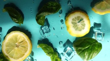 Limon dilimleri, taze fesleğen yaprakları ve buz küpleri parlak mavi bir yüzeye serin ve ferahlatıcı bir yaz atmosferini çağrıştıran içecekler için mükemmel bir şekilde düzenlenmiştir..