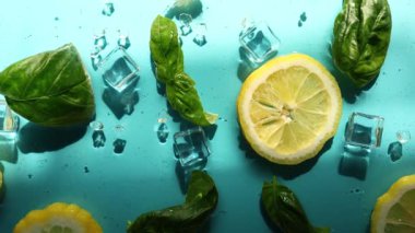 Limon dilimleri, taze fesleğen yaprakları ve buz küpleri parlak mavi bir yüzeye serin ve ferahlatıcı bir yaz atmosferini çağrıştıran içecekler için mükemmel bir şekilde düzenlenmiştir..