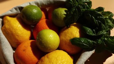 Yeniden kullanılabilir bir sepette canlı sarı limonlar, portakallar ve yeşil limonların yanı sıra taze fesleğen yaprakları, çevre dostu market alışverişi ve sağlıklı yaşam olanakları bulunur..