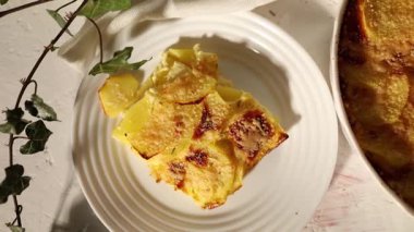 Beyaz bir kırsal mutfak ortamında dilimlenmiş patates ve peynir katmanlarından yapılmış lezzetli rendelenmiş.