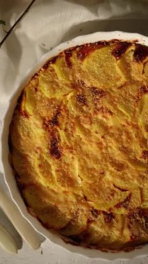 Dikey beyaz bir masada servis edilen altın hamurlu enfes fırınlanmış graten.