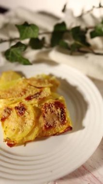 Beyaz bir kırsal mutfakta, dilimlenmiş patates ve peynir katmanlarından yapılmış lezzetli rendelenmiş.