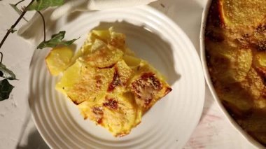 Beyaz bir kırsal mutfak ortamında dilimlenmiş patates ve peynir katmanlarından yapılmış lezzetli rendelenmiş.