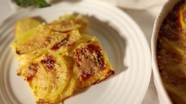 Beyaz bir kırsal mutfak ortamında dilimlenmiş patates ve peynir katmanlarından yapılmış lezzetli rendelenmiş.