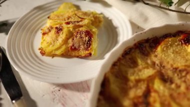 Beyaz bir kırsal mutfak ortamında dilimlenmiş patates ve peynir katmanlarından yapılmış lezzetli rendelenmiş.