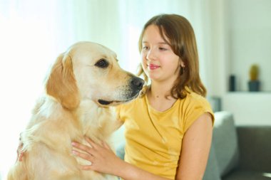 Genç bir kız, Golden Retriever 'ıyla doğal ışıkla dolu parlak, rahat bir oturma odasında kaliteli vakit geçirmekten zevk alır. Birlikte neşeli bir anı paylaşıyorlar..
