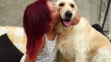 Kırmızı saçlı neşeli bir kız rahat bir arka bahçede Golden Retriever 'ını öpmek için eğiliyor..