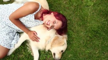 Genç bir kız dost canlısı Golden Retriever 'ına sarılırken yeşil çimlerde dinleniyor. Güneşli bir öğleden sonra bahçede neşeli ve sevgi dolu bir bağ paylaşıyorlar..