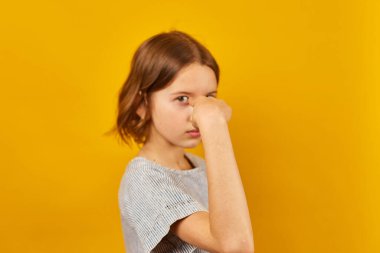 Bir çocuk doğrudan izleyiciye bakarken bir parmağı şakayla işaret eder. Canlı sarı zemin enerji katıyor, eğlenceli ve çekici bir anı yakalıyor..