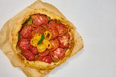 Lezzetli bir domates galeti kağıt üzerinde sergilenir, canlı kırmızı ve sarı domateslerin tabakaları sıcak bir mutfak atmosferinde pullu bir kabuğun üzerinde sergilenir..