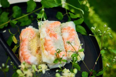 Sebze ve karidesle dolu renkli börekler koyu, yuvarlak bir tepside dizilir. Yemyeşil bitkiler ve narin çiçekler tabağın etrafını sararak canlı bir atmosfer yaratıyor..
