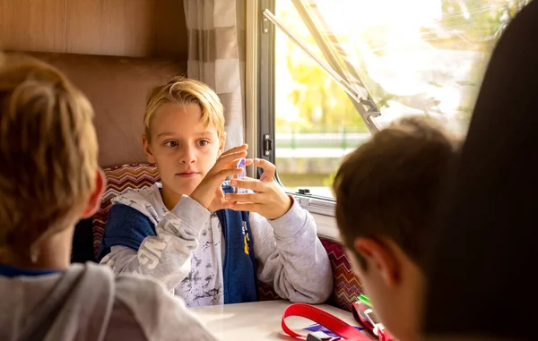 A blond boy playing cards inside the caravan