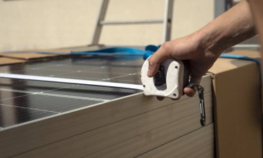 Güneş panelini mezurayla ölçen bir işçinin ellerine yakın çekim.