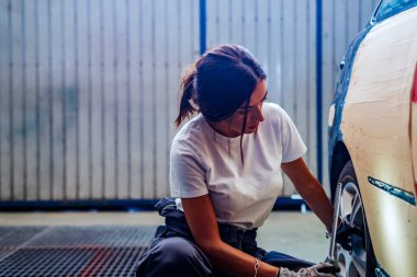 Genç bir kadın tamircinin atölyesinde el feneriyle araba tekerleğini kontrol ediyor. Eşitlik kavramı